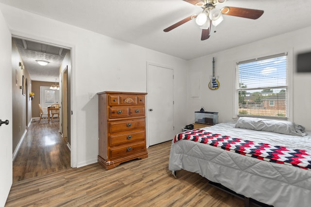bedroom featuring wood finished floors, attic access, baseboards, and a ceiling fan