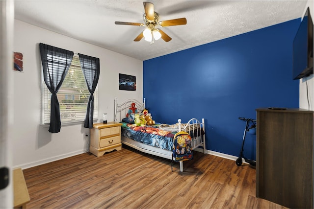 bedroom featuring baseboards, ceiling fan, wood finished floors, and a textured ceiling