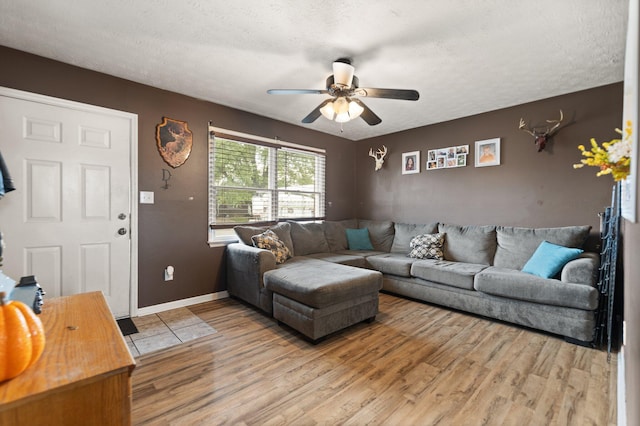 living area featuring baseboards, light wood finished floors, a textured ceiling, and a ceiling fan