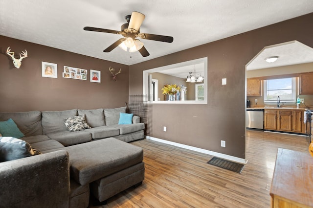 living area featuring baseboards, light wood-type flooring, and ceiling fan with notable chandelier