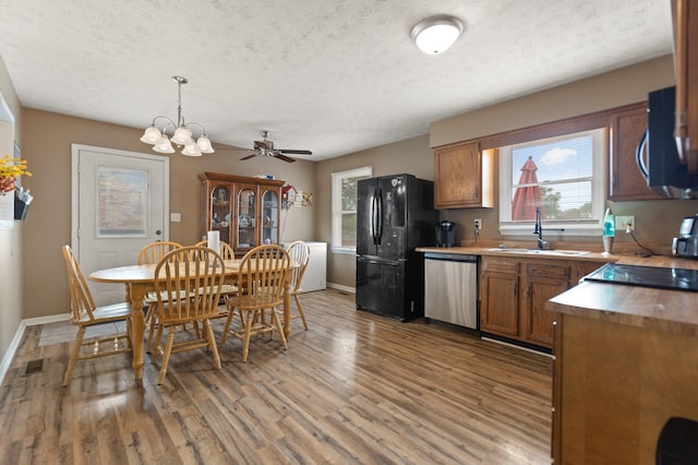 kitchen featuring a textured ceiling, black appliances, brown cabinets, light wood finished floors, and a sink