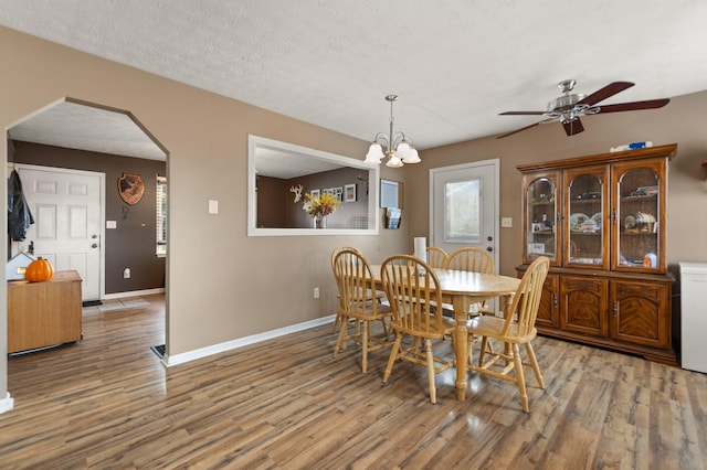 dining space with arched walkways, ceiling fan with notable chandelier, a textured ceiling, and wood finished floors