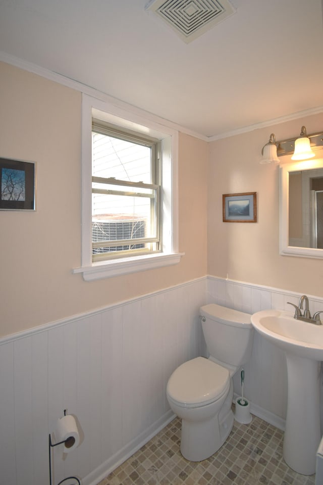 half bathroom with visible vents, toilet, tile patterned floors, and wainscoting