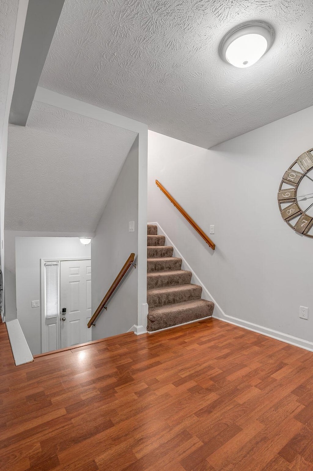 stairway featuring a textured ceiling, baseboards, and wood finished floors