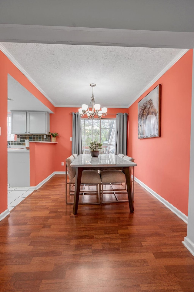 unfurnished dining area featuring a textured ceiling, ornamental molding, a chandelier, wood finished floors, and baseboards