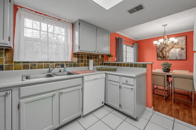 kitchen featuring an inviting chandelier, a peninsula, visible vents, dishwasher, and a sink