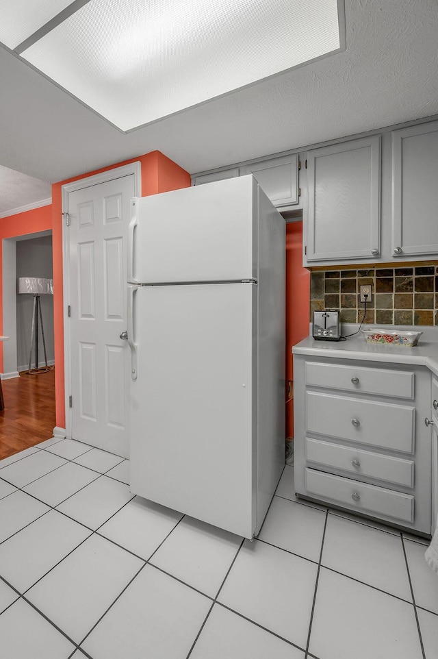 kitchen featuring freestanding refrigerator, light tile patterned flooring, light countertops, decorative backsplash, and gray cabinetry