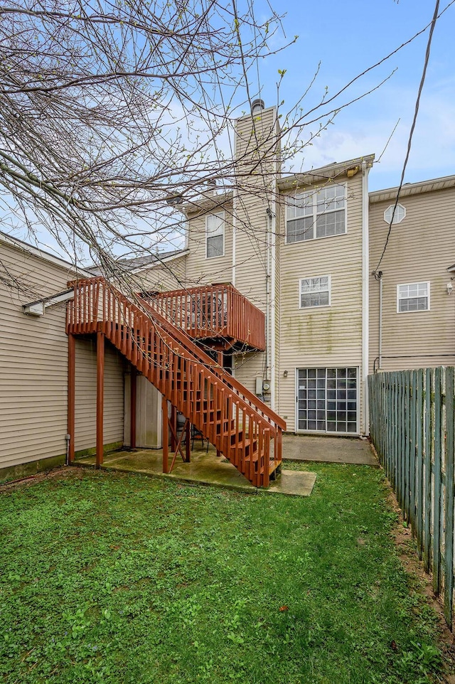 back of house featuring a wooden deck, a lawn, stairway, fence, and a chimney