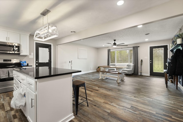kitchen featuring dark countertops, a kitchen island, dark wood-type flooring, a breakfast bar area, and appliances with stainless steel finishes