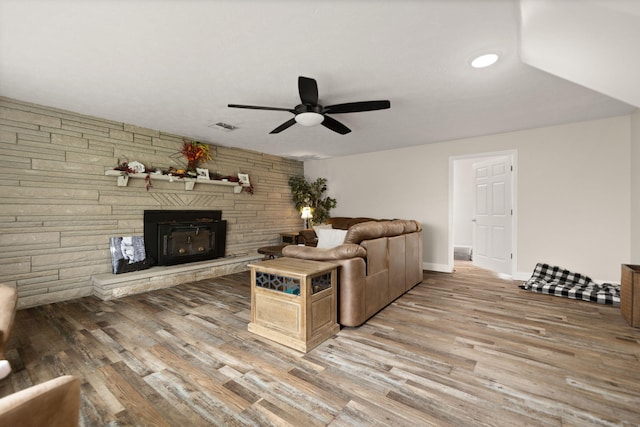 living area with visible vents, baseboards, a stone fireplace, a ceiling fan, and light wood-style flooring