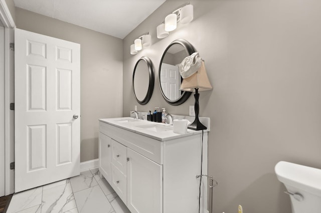bathroom featuring toilet, double vanity, marble finish floor, and a sink