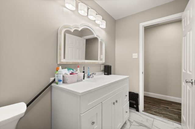 half bath featuring toilet, marble finish floor, baseboards, and vanity