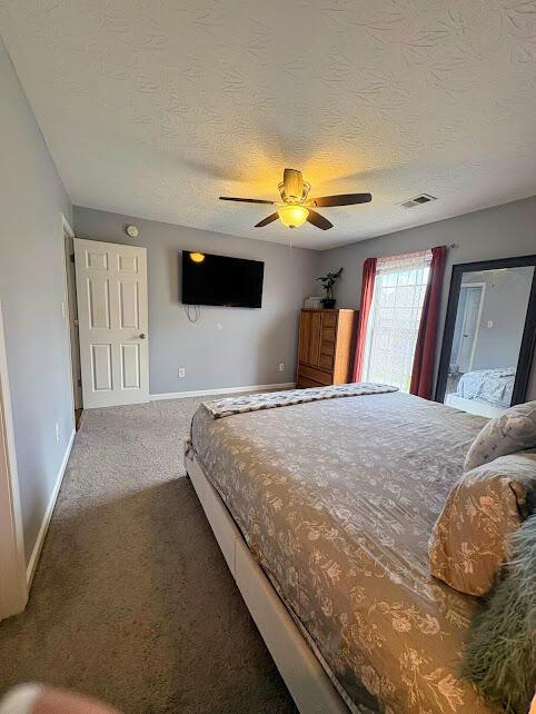 carpeted bedroom featuring baseboards, visible vents, a textured ceiling, and ceiling fan