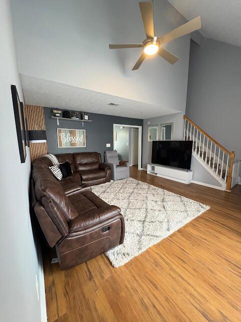 living room with stairway, wood finished floors, high vaulted ceiling, and ceiling fan
