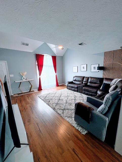 living area featuring lofted ceiling, wood finished floors, visible vents, and a textured ceiling