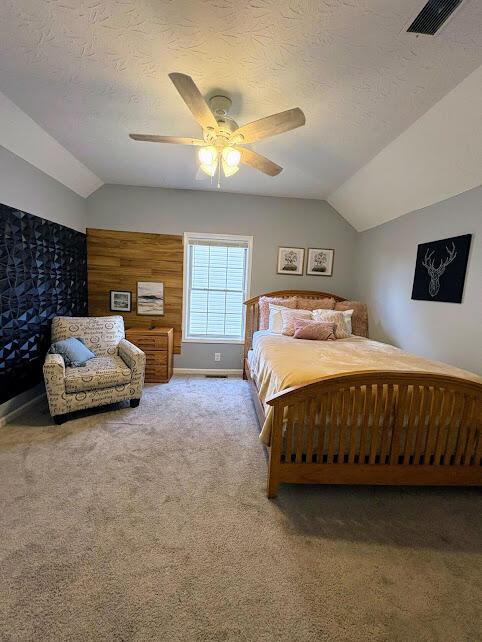 carpeted bedroom with a textured ceiling, vaulted ceiling, visible vents, and a ceiling fan