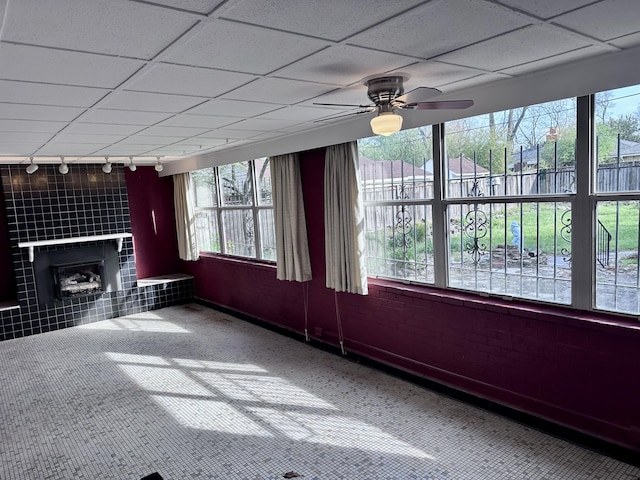 unfurnished living room featuring a ceiling fan, a tile fireplace, a drop ceiling, and carpet