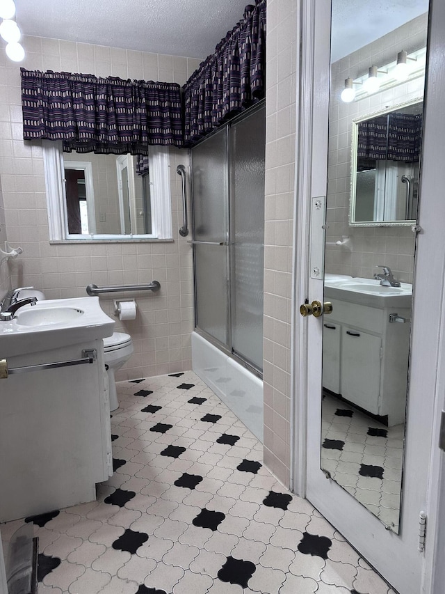 bathroom with bath / shower combo with glass door, toilet, tile walls, backsplash, and vanity