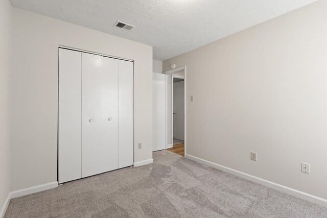 unfurnished bedroom featuring a textured ceiling, a closet, visible vents, carpet floors, and baseboards