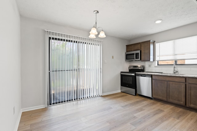 kitchen featuring baseboards, a sink, appliances with stainless steel finishes, a chandelier, and light wood-style flooring