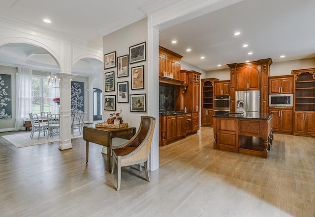 kitchen with decorative columns, brown cabinetry, arched walkways, stainless steel appliances, and light wood finished floors
