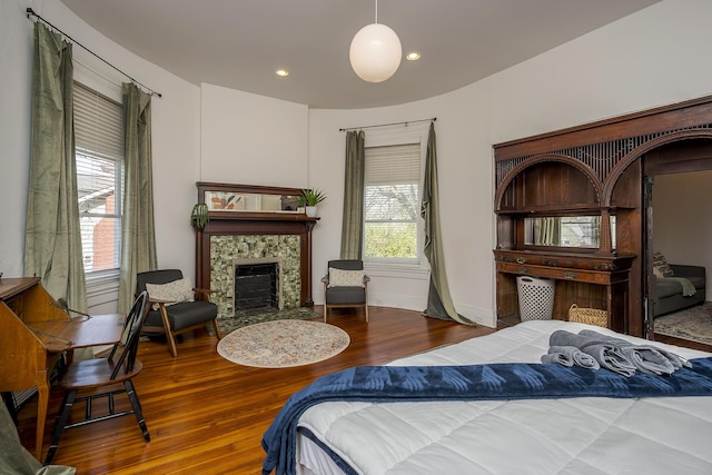 bedroom featuring recessed lighting, a tiled fireplace, baseboards, and wood finished floors