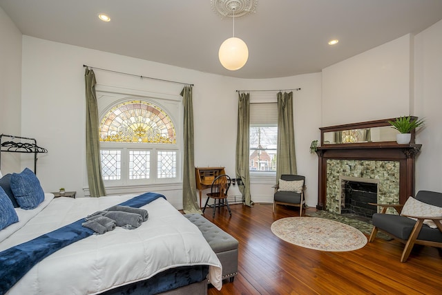 bedroom with wood finished floors, baseboards, a stone fireplace, and recessed lighting