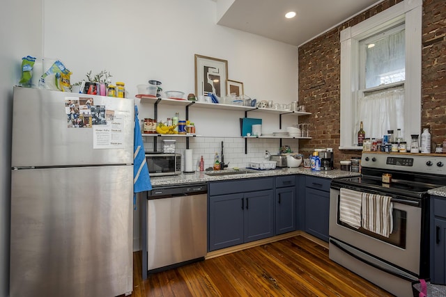 kitchen with appliances with stainless steel finishes, brick wall, open shelves, dark wood finished floors, and a sink
