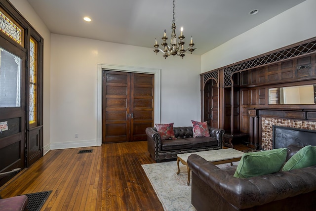 living area featuring baseboards, an inviting chandelier, a brick fireplace, visible vents, and hardwood / wood-style flooring