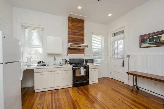 kitchen featuring freestanding refrigerator, electric range, light countertops, a sink, and wood-type flooring