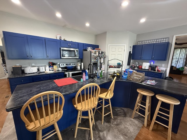 kitchen featuring dark countertops, appliances with stainless steel finishes, blue cabinetry, and a sink