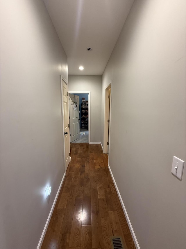 hallway featuring dark wood-type flooring, baseboards, and visible vents