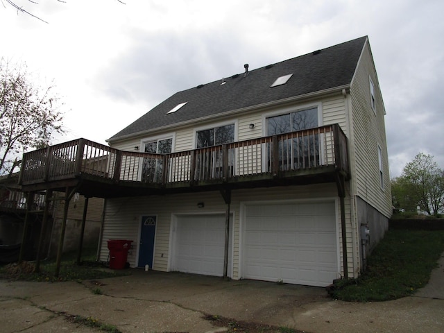 back of property with a deck, roof with shingles, an attached garage, and driveway