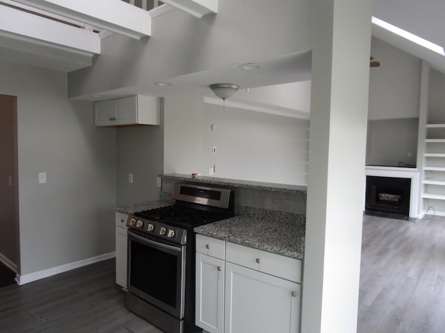 kitchen featuring stainless steel gas range, baseboards, light stone counters, dark wood finished floors, and white cabinetry