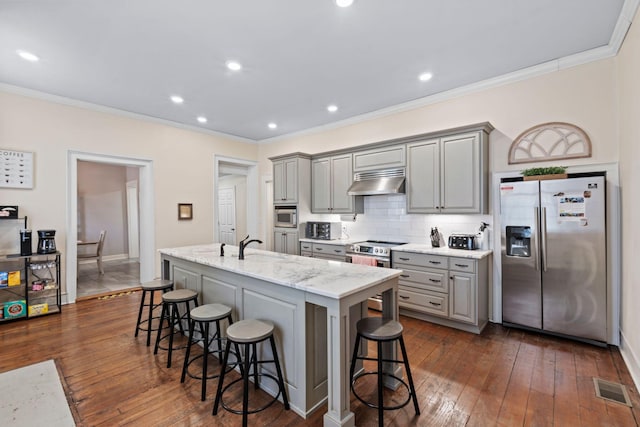 kitchen featuring gray cabinets, under cabinet range hood, visible vents, a breakfast bar area, and appliances with stainless steel finishes