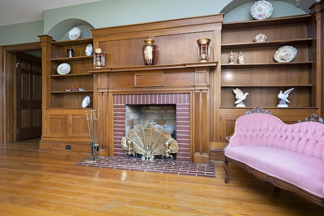 living area featuring built in shelves, a brick fireplace, and wood finished floors