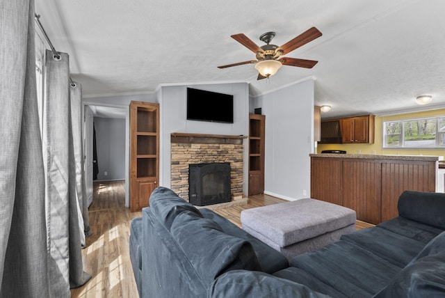living area featuring lofted ceiling, a ceiling fan, a stone fireplace, and a textured ceiling