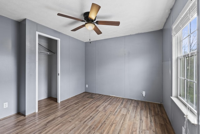 unfurnished bedroom with wood finished floors, a closet, ceiling fan, and multiple windows