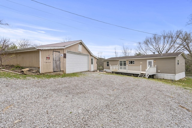 back of property with a detached garage, an outbuilding, driveway, and a deck