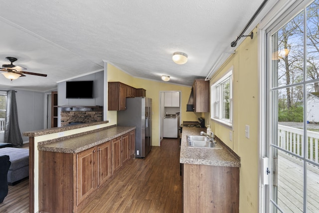 kitchen with a stone fireplace, a sink, open floor plan, stainless steel refrigerator with ice dispenser, and dark wood-style floors