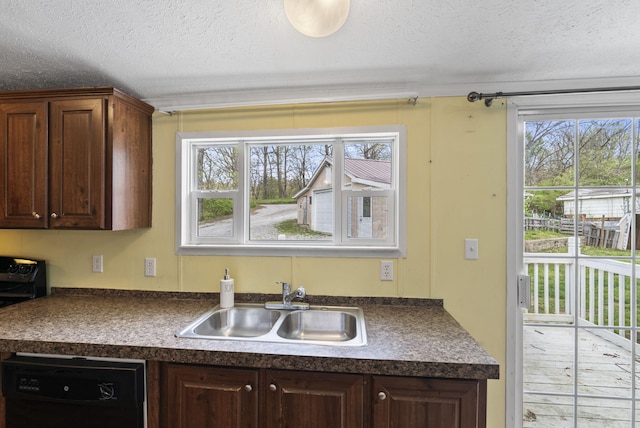 kitchen with dark countertops, dishwasher, a sink, and a textured ceiling