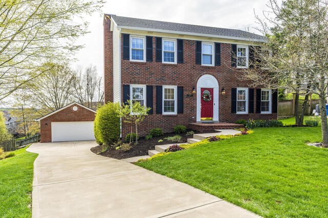 colonial home with a detached garage, a front lawn, fence, an outbuilding, and brick siding