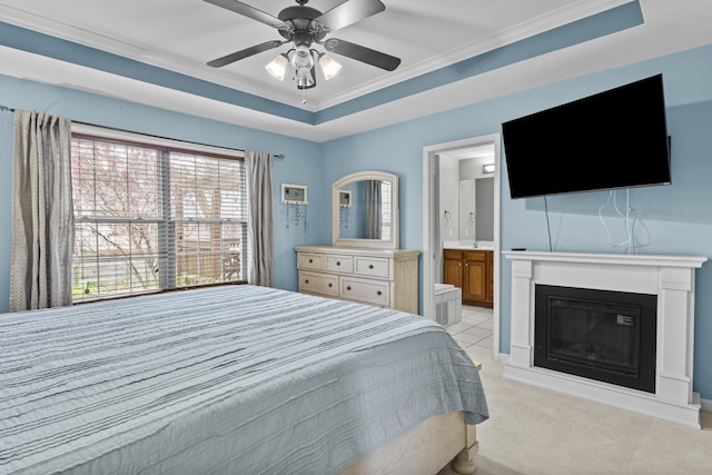 bedroom featuring a glass covered fireplace, light colored carpet, ensuite bathroom, a raised ceiling, and crown molding