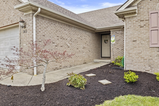 entrance to property featuring an attached garage, roof with shingles, and brick siding