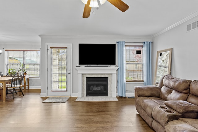 living room featuring ceiling fan, ornamental molding, wood finished floors, a tiled fireplace, and baseboards