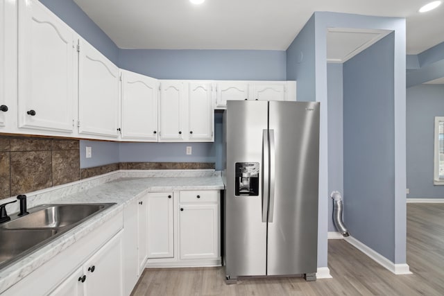 kitchen featuring stainless steel fridge with ice dispenser, light wood-type flooring, white cabinetry, a sink, and baseboards