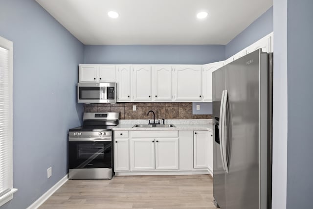 kitchen with white cabinets, appliances with stainless steel finishes, a sink, light wood finished floors, and backsplash