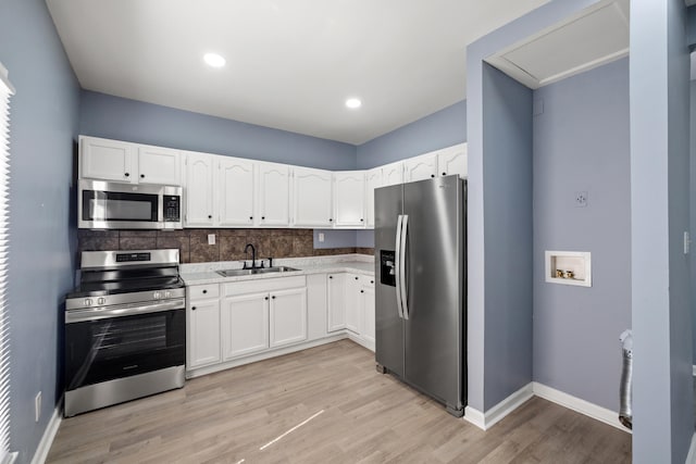 kitchen featuring light wood-type flooring, white cabinets, a sink, stainless steel appliances, and decorative backsplash