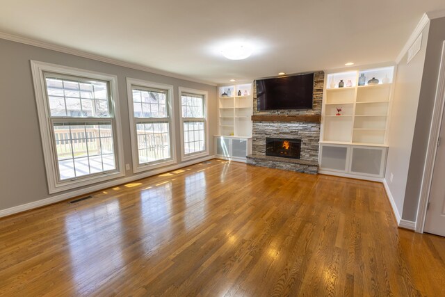 unfurnished living room with a fireplace, ornamental molding, visible vents, wood finished floors, and baseboards