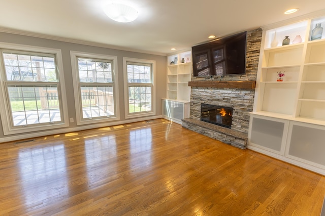 unfurnished living room with a stone fireplace, built in features, ornamental molding, visible vents, and wood finished floors